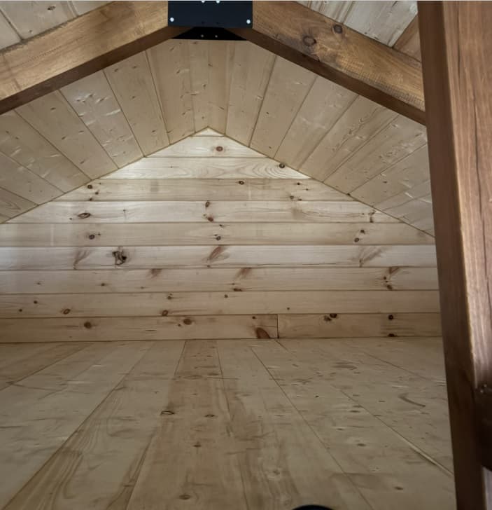 Log cabin loft interior with light pine wood paneling and exposed dark wood beams