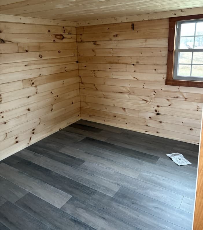 Small wood-paneled room with gray vinyl flooring and natural light from window