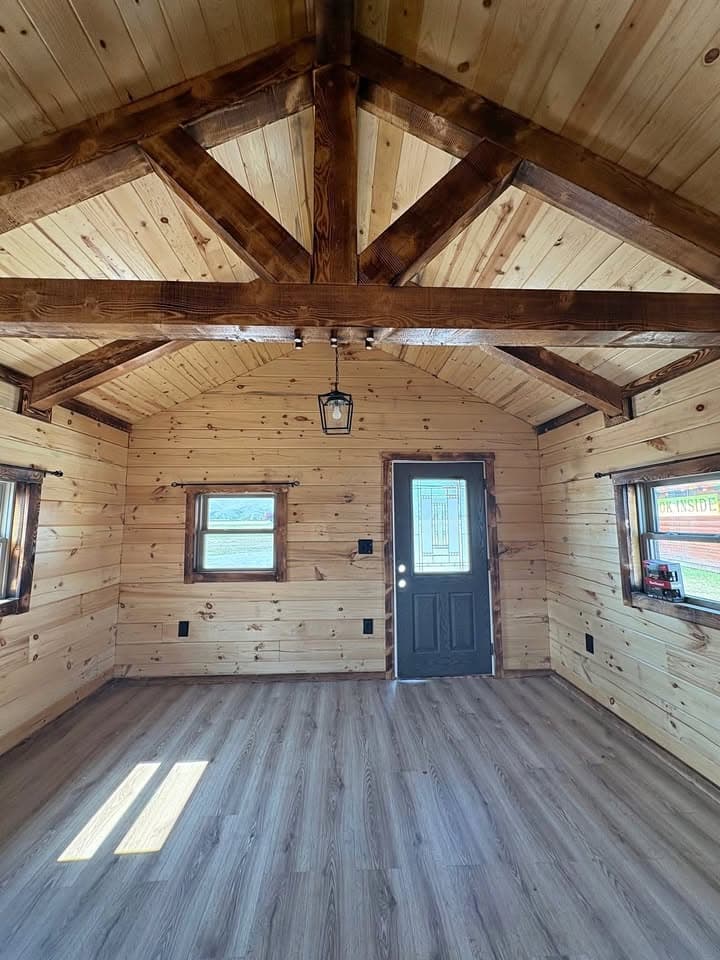 Vaulted log cabin interior with exposed beams, entry door with decorative glass panel, and spacious open floor plan