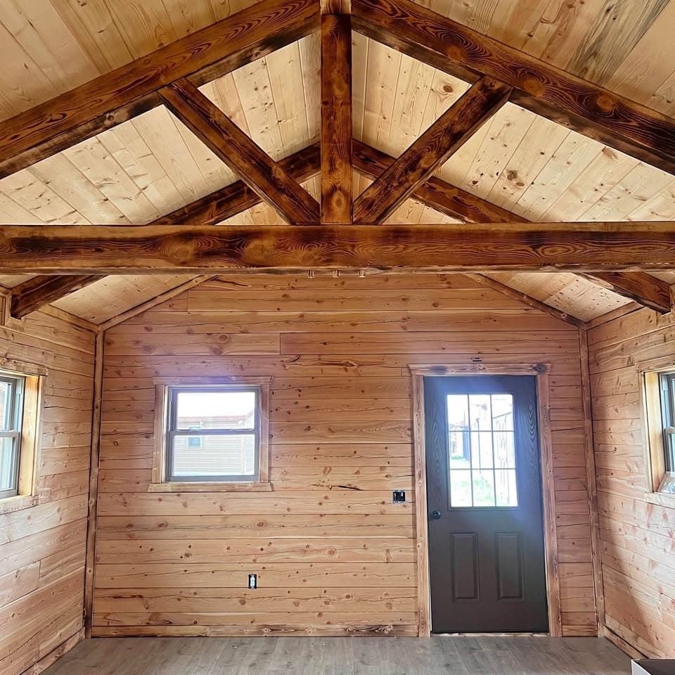 Wood cabin interior with vaulted ceiling, exposed beams, and dark entry door with window